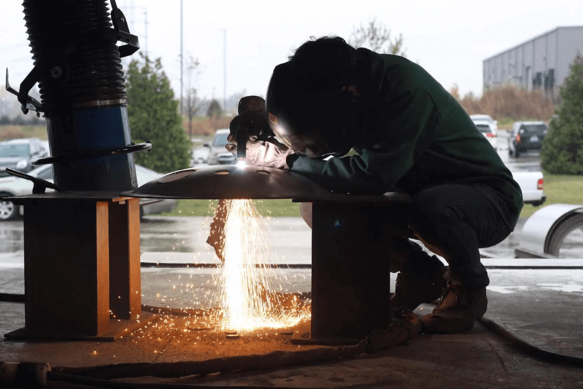 An MXD Process welder welding a round tank lid outside in a shop.